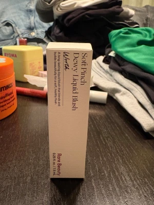 Rare Beauty Soft Pinch Dewy Liquid Blush - Rare Beauty Soft Pinch Dewy Liquid Blush i nyansen Worth. Flytande rouge som ger en fräsch, daggig finish och smälter in i huden. Kommer i en stilren beige kartong, 7,5 ml. Perfekt för att skapa en naturlig glow med enkel applicering.