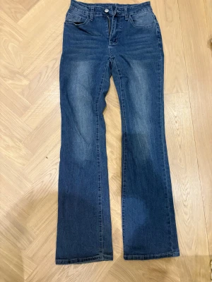 Blå bootcut jeans från SHEIN - Snygga blå jeans från SHEIN i bootcut-modell med klassisk femficksdesign och hög midja. Jeansen har en lätt tvättad look och är tillverkade i stretchigt bomullsmaterial för skön passform. Perfekta för dig som gillar retrovibbar och vill ha ett par jeans med lite vidare ben.