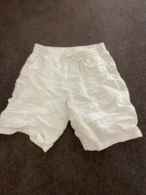 Beiga linneshorts från RYVLS med snörning - Fräscha vita shorts från RYVLS i mjukt linne. De har elastisk midja med snörning och fickor på sidorna. Perfekt för chill dagar och sommarhäng. Lätta och luftiga med avslappnad passform.