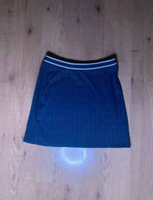 Mörkblå kortkjol med sportig midja - Snygg mörkblå kortkjol med diskret mönster och sportig känsla tack vare den elastiska midjan med vita ränder. Kjolen har en rak passform och är perfekt för dig som gillar en stilren och enkel look.