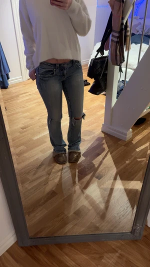 Miss Me ljusblå bootcut jeans strl 27 - Säljer ett par ljusblå Miss Me jeans med bootcut och låg midja. Jeansen har slitningar och hål vid knäna och ett litet hål under fickan , snygga detaljer med dekorativa nitar och broderade sömmar. Klassisk femficksmodell i mjukt denimtyg, perfekta för en avslappnad look.