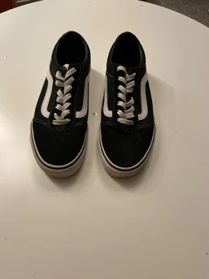 Svarta Vans Old Skool sneakers strl 42 - Klassiska Vans Old Skool sneakers i svart med vit sula och vit sidostrip. Skorna har snörning, rund tå och är tillverkade i en mix av mocka och canvas. Perfekta för en streetwear-look och funkar året runt. Jag köpte skorna för 999kr och säljer nu för 550kr