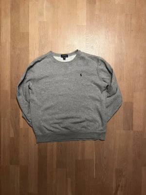 Grå sweatshirt från Polo Ralph Lauren - En stilren grå sweatshirt från Polo Ralph Lauren i storlek XL/18-20 men sitter bra som M. Tröjan har rund hals, långärmade ärmar och klassisk broderad logga på bröstet. Tillverkad i mjuk bomullsmix som är skön mot huden. Perfekt för chill dagar och enkel att matcha med jeans eller joggers.  Skick 9/10 ✅ Skickar inom 48 timmar om inte samma dag 🚚