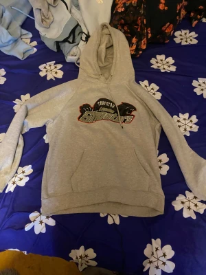 Grå hoodie Trapstar Shooters - Säljer en grå hoodie från Trapstar med fet Shooters-tryck på bröstet och svarta detaljer. Tröjan har huva med snörning och en stor magficka. Perfekt för dig som gillar streetwear och vill ha en chill look.