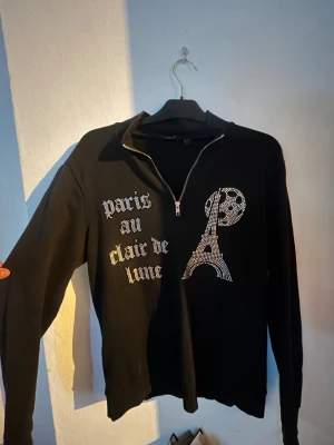 Läs beskrivningen Svart tröja half zip - Svart långärmad tröja med strassdetaljer som bildar texten 'paris au clair de lune' och motiv av Eiffeltornet och måne. Säljer tröjan då jag inte gillar den så mycke så använder den aldrig skriv ett bud:) har för mig tröjan kostar 700-800 ny