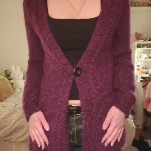 Lila kofta med stor knapp - Stickad mysig lila kofta med lång ärm och en stor knapp framtill.