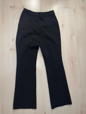Svarta bootcut kostymbyxor - Snygga svarta kostymbyxor med bootcut-ben och klassisk passform. Byxorna har hällor för bälte, fickor fram och bak samt pressveck längs benen. Perfekta för en stilren look och passar till många olika outfits.