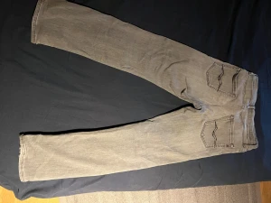 Replay grå jeans straight fit - Säljer ett par gråa jeans från Replay med klassisk straight fit och snygga svarta detaljer på bakfickorna. Jeansen har normal passform, fem fickor och är tillverkade i mjukt jeanstyg. Perfekt för dig som gillar stilrena och tidlösa jeans.