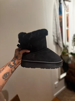 Svarta ”uggs”  med päls och rosett bak  -  svarta uggs med fluffig päls runt skaftet och söta rosetter bak. Använda fåtal gånger, därför säljer jag dom. Strlk 40, men sitter mer som 39. Köpta för 499, säljer för 200