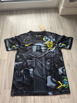 Brazil X Rio De Janeiro Fotbollströja (BLACK WEEKEND RABATT) - Unik svart Brasilien fotbollströja från Nike med detaljerat grafiskt mönster, Kristusstatyn och brasilianska flaggan. Gula och blå accenter, Brasil-märke på bröstet och Dri-Fit material som andas. Rund hals och korta ärmar, perfekt för dig som vill sticka ut på planen.