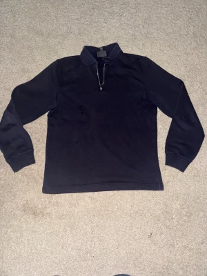 Mörkblå half zip tröja från H&M - Snygg mörkblå långärmad tröja från H&M med regular fit. Tröjan har en klassisk krage och half zip-dragkedja framtill. Materialet är mjukt och känns som bomull, perfekt för kyliga dagar. Passar dig som gillar enkel och stilren look.