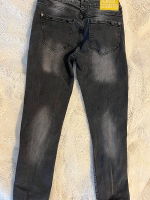 Svarta Dsquared2 jeans med färgstänk - Snygga svarta jeans från Dsquared2 med coola slitningar och färgstänk i vitt och gult på framsidan. Modellen har fyra fickor, gul Dsquared2-tag och en stor gul patch med texten 'Caten Heated' bak. Jeansen har en smal passform och är tillverkade i klassiskt jeansmaterial.