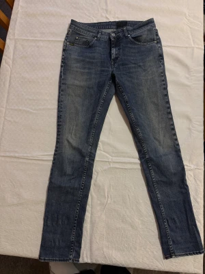 Blå jeans från Tiger of Sweden - Snygga blå jeans från Tiger of Sweden med klassisk femficksdesign och diskret tvättad look. Jeansen har raka ben och normal passform, tillverkade i mjukt bomullsjeansmaterial. Perfekta för dig som gillar stilrena och tidlösa jeans.