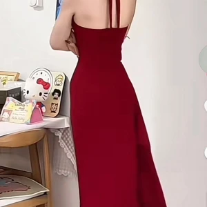 Vinröd långklänning med hög slits  - Supersnygg vinröd långklänning med halterneck och djup slits framtill. Klänningen har en dekorativ ros vid urringningen och en figurnära passform som framhäver siluetten. Perfekt för dig som vill sticka ut med en elegant och trendig look.