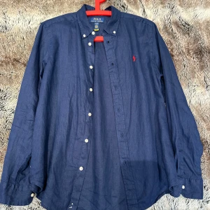 Mörkblå linneskjorta Polo Ralph Lauren - Snygg mörkblå skjorta från Polo Ralph Lauren i linne. Tröjan är inprinsip helt ny och har absolut inga skavanker. Köpt på kidsbrandstore orginal pris 1000. Priset är ej hugget i sten!