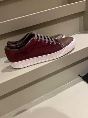 Vinröda lanvins  - Snygga vinröda lanvins  med ovandel i mocka och  gröna detaljer i skinn på tå och runt kanten. Skorna har grå snörning och vit platt sula som ger en clean look. Perfekt för dig som gillar stilrena och unika sneakers med lite extra attityd.