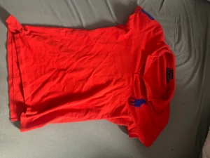 Röd Ralph Lauren Skinny Polo M - Snygg röd pikétröja från Ralph Lauren i modellen The Skinny Polo. Tröjan har korta ärmar, klassisk krage och blått broderat logomärke på bröstet. Tillverkad i mjuk bomull som är skön mot huden. Perfekt för dig som gillar stilrena och sportiga plagg.