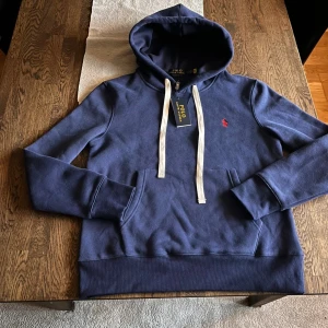 Blå Ralph Lauren Hoodie - Tja, säljer en blå Ralph Lauren hoodie då jag fick den när jag fyllde år men den passade inte och returrätten har gått ut tråkigt nog. Den är storlek S men skulle väl eventuellt passa M om du är lite smalare eller bara vill ha en lite mer åtsittande och tajtare passform. Passar alltså främst personer som är S och XS. Tveka inte på att höra av dig om du har frågor!😃
