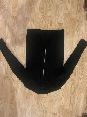 Svart ribbad stickad tröja med dragkedja - Svart långärmad stickad tröja med ribbad struktur och snygg dragkedja framtill. Tröjan har en klassisk passform och är perfekt för dig som gillar stilrena och enkla plagg. Passar dig som vill ha en basic men ändå trendig look.