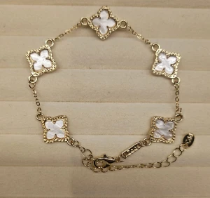 Guldfärgat armband med vita fyrklöver - Snyggt armband i guld med fem fyrklöverformade länkar i vit pärlemor. Kedjan är tunn och har justerbar längd med karbinlås. Perfekt för dig som gillar eleganta och unika detaljer. Fyrklöverdesignen ger en lyxig och trendig vibe✨️🫶.
