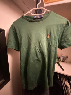 Grön t-shirt från Polo Ralph Lauren - Snygg grön t-shirt från Polo Ralph Lauren med klassisk broderad logga på bröstet. Modellen är custom slim fit och har rund hals samt korta ärmar. Tillverkad i mjuk bomull som känns skön mot huden. Perfekt för dig som gillar stilrena och tidlösa plagg.