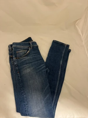 Blå jeans från Tiger of Sweden - Snygga blå jeans från Tiger of Sweden med klassisk femficksdesign och ljusa slitningar framtill. Jeansen har normal passform, raka ben och är tillverkade i mjukt denimtyg med en skön stretch. Perfekt för dig som gillar stilrena och tidlösa jeans.