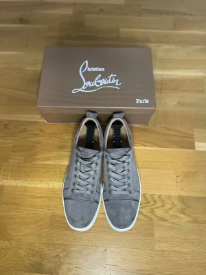Christian Louboutin Gråa - Snygga grå sneakers från Christian Louboutin i mjuk mocka med klassisk vit sula och ikonisk röd undersida. Skorna har rund tå, snörning och diskret branding. Perfekta för dig som vill ha en lyxig och stilren look med en touch av Paris.
