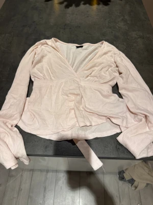Ljusrosa omlottblus från Gina Tricot - Säljer en ljusrosa omlottblus från Gina Tricot med långa ärmar och v-ringad hals. Blusen har ett knytband i midjan och är tillverkad i mjuk bomull. Perfekt för dig som gillar romantisk och feminin stil.💞💞