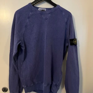 Blå sweatshirt från Stone Island - Säljer en blå långärmad sweatshirt från Stone Island med klassisk patch på vänster arm. Tröjan är inte använd mycket men har dessvärre blivit urtvättad, därav det låga priset. (Äkthetsbevis medföljer)