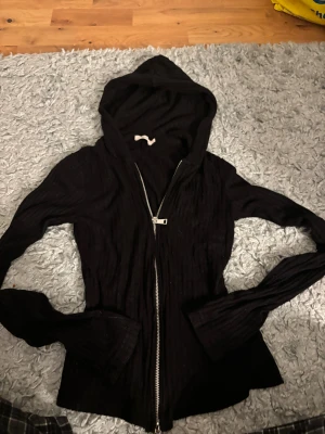 Svart ribbad hoodie från Nelly XS - Svart hoodie från Nelly i storlek XS med ribbad struktur och lång ärm. Tröjan har huva och en snygg dragkedja framtill som gör den enkel att ta på och av. Perfekt för dig som gillar en stilren och bekväm look.🖤🖤