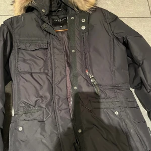 Svart dunjacka med fuskpäls från Hollies - Ordinarie pris är 4000 kr. Pris kan diskuteras vid snabba affärer. Svart dunjacka från Hollies med snygg fuskpäls på huvan. Jackan har flera fickor framtill, dragkedja och tryckknappar. Perfekt för kalla dagar och har en klassisk, stilren look som funkar till allt.