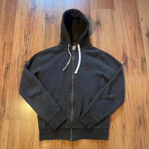 Mörkgrå hoodie från Polo Ralph Lauren - Snygg mörkgrå hoodie från Polo Ralph Lauren med dragkedja och vit snörning i huvan. Size S/170. Längd 62 cm, bredd 50 cm, ärmlängd 59 cm. Mycket bra skick men finns en liten fläck på baksidan 🫟 