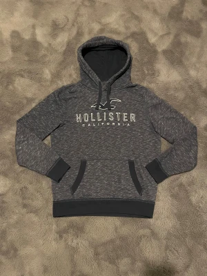 Mörkblå hoodie från Hollister - 🔥 PRIS ELLER BYTEN KAN ALLTID DISKUTERAS!!!! 🔥                                                   Snygg mörkblå/grå hoodie från Hollister med vit logotyp och text på bröstet. Tröjan har huva med snörning, ribbade muddar och magficka. ⭐ 
