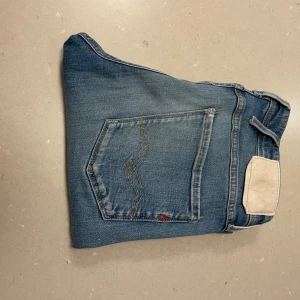 Replay Anbass blå jeans slim fit - Snygga Replay Anbass jeans i klassisk blå tvätt med slim fit. Jeansen har fem fickor, ljusare slitningar och detaljerade sömmar på bakfickan. Tillverkade i jeansmaterial med knapp och dragkedja framtill. Perfekt för dig som gillar stilrena och moderna jeans. W32 L32