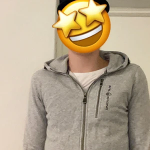 Grå hoodie från Sail Racing - Säljer en grå hoodie från Sail Racing med dragkedja framtill och en extra zip på bröstet. Tröjan har huva, lång ärm och snyggt broderad logga på vänster sida. Perfekt för chill dagar och enkel att matcha med jeans eller joggers.