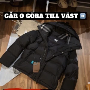 Burrberry Jacka - Svart dunväst från Burberry med avtagbara ärmar och huva. Insidan har klassiskt Burberry-rutigt foder vid huvan. Västen har dragkedja och knappar framtill samt praktiska fickor. Perfekt för dig som vill ha några exktra blickar på stan.Storlek S passar för M också
