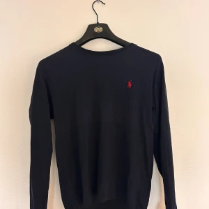 Mörkblå långärmad tröja Polo Ralph Lauren - Snygg mörkblå långärmad tröja från Polo Ralph Lauren i storlek XS men passar verkligen S. Tröjan har en klassisk rund hals och det ikoniska röda Polo-logot på bröstet. Tillverkad i mjuk bomull som är skön mot huden och passar perfekt till jeans eller chinos.