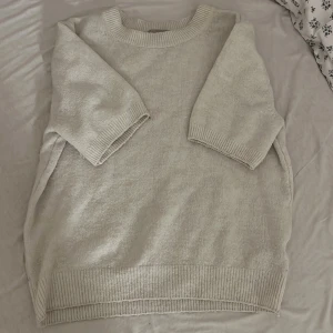 Beige stickad tröja från H&M - Mysig beige stickad tröja från H&M med ribbade detaljer vid hals, ärmslut och nederkant. Tröjan har en avslappnad passform och trekvartsärmar, perfekt för lager-på-lager under kyliga dagar. Enkel och stilren design som funkar till många olika looks.