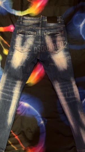 Dsquared2 blå skinny jeans med tryck - Snygga blå jeans från Dsquared2 med blekta detaljer och stort DSQUARED2-tryck både fram och bak. Skinny fit med klassisk femficksdesign, knappgylf och coolt sliten look. Perfekt för dig som gillar streetstyle och vill sticka ut.