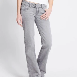Grå bootcut jeans med broderade fickor - Snygga grå jeans med bootcut passform och låg midja. Jeansen har klassisk femficksdesign och coolt broderi på bakfickorna. Tillverkade i mjukt jeanstyg som ger en skön känsla. Perfekta för dig som gillar detaljer och vill sticka ut lite extra. Helt oanvända!