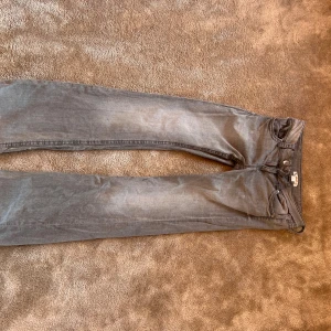 Grå jeans med bootcut passform. - Säljer ett par grå jeans med klassisk femficksdesign och bootcut ben. Jeansen har knappstängning fram och snygga detaljer på bakfickorna. Perfekt för dig som gillar en enkel och stilren look.