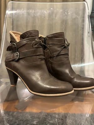 Bruna skinnstövletter från Lea Foscati - Snygga bruna stövletter i äkta skinn från italienska Lea Foscati. Modellen har rund tå, hög klack, snörning framtill, dubbla spännen och dragkedja på sidan. Perfekta för dig som vill ha en stilren och elegant look med lite edge.