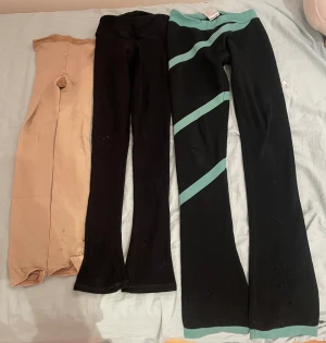Tre par leggings i olika färger - Säljer tre par leggings: ett par beige, ett par helsvarta och ett par svarta med turkosa detaljer. Alla har hög midja och är i stretchigt syntetmaterial, perfekta för träning eller chill. De svarta med turkosa ränder har en cool sportig look.
