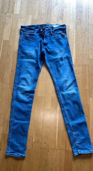 Replay Anbass blå jeans slim fit - Snygga Replay Anbass jeans i klassisk blå färg med slim fit och raka ben. Jeansen är aldrig använda. Jeansen har fem fickor, dragkedja och knappstängning. Materialet är stretchigt jeans för skön passform. Perfekt för dig som gillar stilrena och moderna jeans.