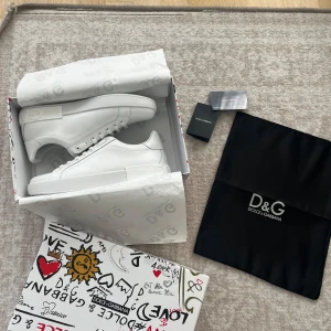 Vita sneakers från Dolce & Gabbana - Stilrena helvita sneakers i skinn med diskret logga på hälen och klassisk snörning. Skorna är köpte från plick men ej äkta tror jag och priset går att diskuteras. Snygg minimalistisk design med rund tå och platt sula, perfekta för en clean och modern look.                                   Obs ej någon kvitto, plus ej riktiga av vad jag misstänker som nämnt tidigare.