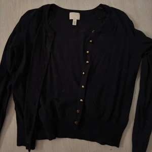Mörkblå kofta med guldfärgade knappar - Mörkblå kofta från H&M i storlek M med långa ärmar och guldfärgade knappar framtill. Använd fåtal gånger 