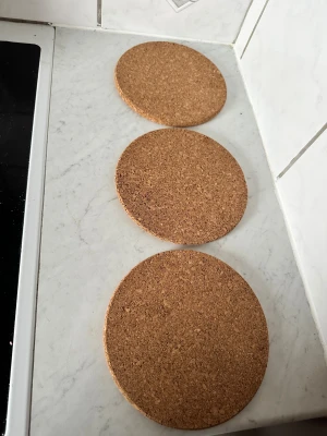 Underlägg för grytor eller annat  - Bilderna visar tre runda grytunderlägg i kork. De är i gott skick utan synligt slitage eller skador. Perfekta för att skydda bord och bänkar från varma kastruller och grytor. Lätta, hållbara och enkla att rengöra. Passar utmärkt i köket eller på matbordet.Underlägg för köket.