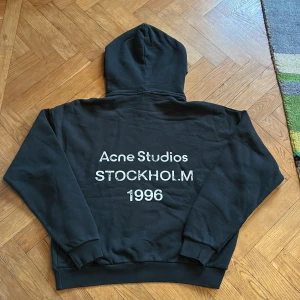 Svart hoodie Acne Studios Stockholm - Svart hoodie från Acne Studios med stor vit text på ryggen: 'Acne Studios STOCKHOLM 1996'. Riktigt fet och efterfrågad! Skriv om frågor om pris eller hoodien. Skickar inom 1 dag!