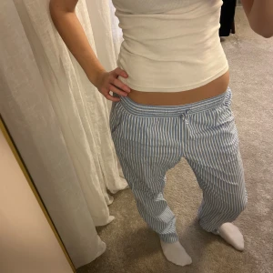 Blåvit randiga pyjamasbyxor med snörning - Säljer ett par chill blåvit randiga pyjamasbyxor med snörning i midjan. De har en relaxed passform och är perfekta för att hänga hemma eller dra till stranden. Byxorna har fickor på sidorna och är gjorda i ett lätt och luftigt material.