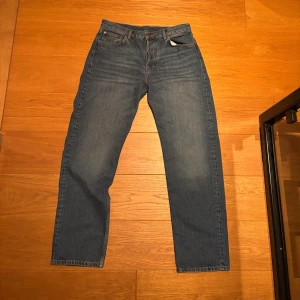 Blå jeans från J.Lindeberg 34/32 - Snygga blå jeans från J.Lindeberg i klassisk straight fit med fem fickor och bruna detaljer på bakfickan. Jeansen har orange sömmar och är tillverkade i slitstarkt denim. Perfekt passform för dig som gillar en tidlös look.